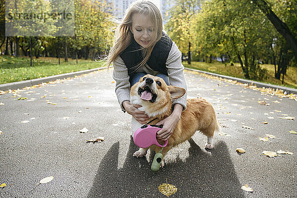 Frau passt Hundeleine auf der Straße im Herbstpark an