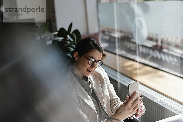 Geschäftsfrau mit Brille macht im Büro ein Selfie mit dem Mobiltelefon