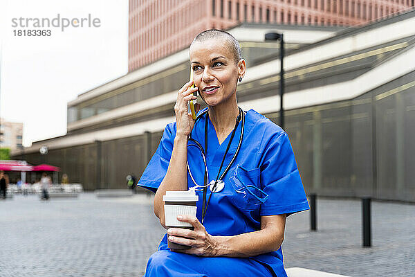 Lächelnde Krankenschwester mit Einwegkaffeetasse  die auf dem Handy spricht