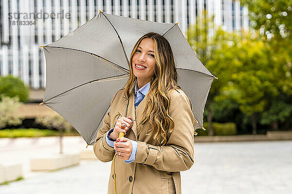 Lächelnde Geschäftsfrau mit Regenschirm vor Bürogebäude
