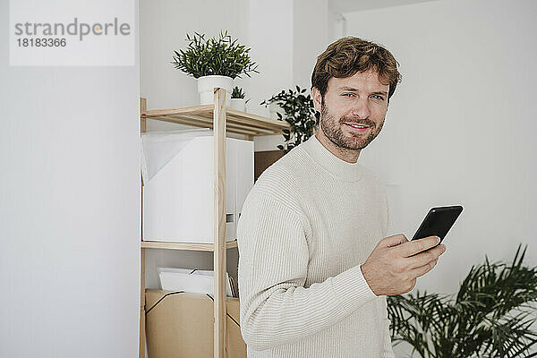 Lächelnder Geschäftsmann mit Smartphone am Arbeitsplatz