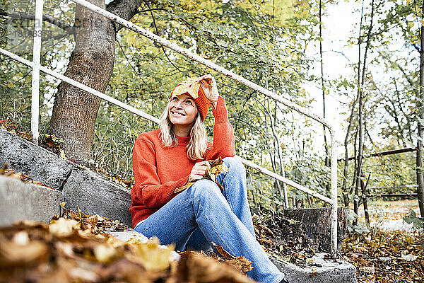 Lächelnde Frau mit Herbstblatt  die im Park träumt