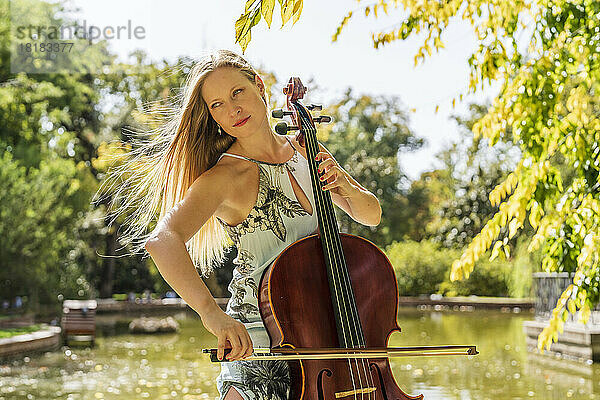 Blonde Frau spielt Cello vor einem See im Park