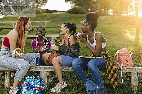 Fröhliche Freunde beim Snacken auf der Bank im Park