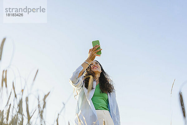 Glückliche Frau benutzt Smartphone im Feld unter klarem Himmel