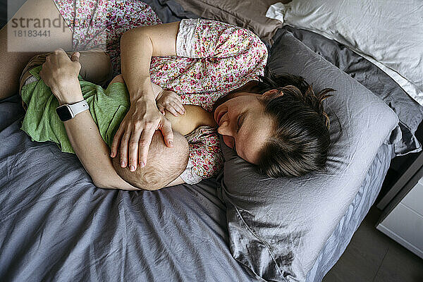 Mother breastfeeding boy lying on bed at home
