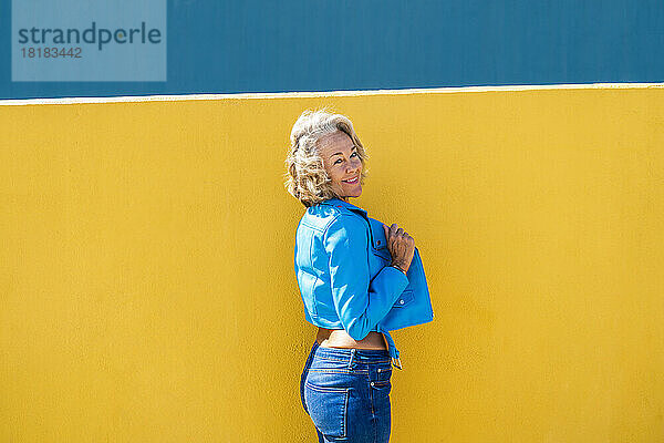 Lächelnde Frau in blauer Lederjacke vor der Wand