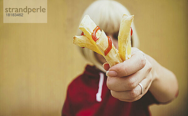 Frau zeigt Pommes Frites mit Ketchup vors Gesicht