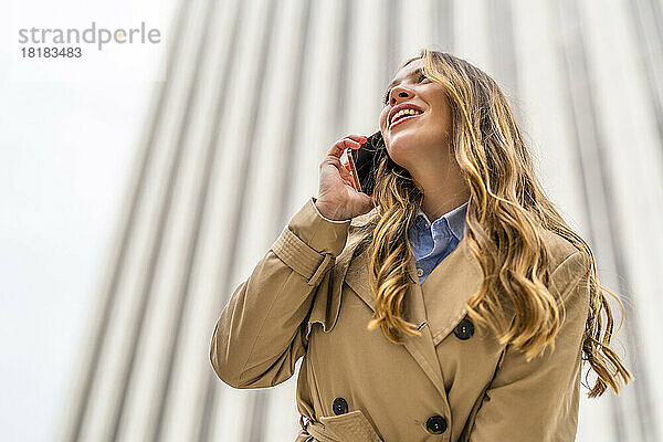 Glückliche Geschäftsfrau  die vor dem Gebäude mit dem Handy telefoniert