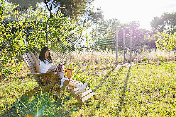 Reife Frau liest an einem sonnigen Tag im Hinterhof ein Buch