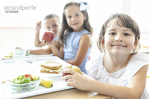 Lächelnder Grundschüler mit Essenstablett auf dem Tisch in der Mittagspause in der Cafeteria