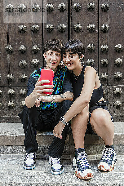Lächelnder Mann mit Freundin macht Selfie mit dem Handy vor der Tür
