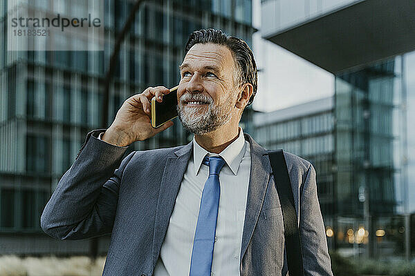 Nachdenklicher reifer Geschäftsmann  der vor dem Gebäude mit dem Smartphone spricht