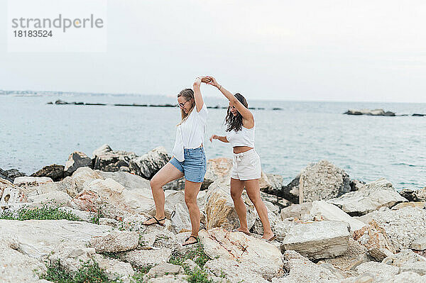 Freunde halten sich an den Händen und gehen gemeinsam auf einem Felsen am Strand spazieren