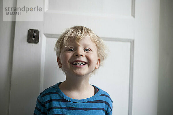 Portrait of laughing little boy in front of white door