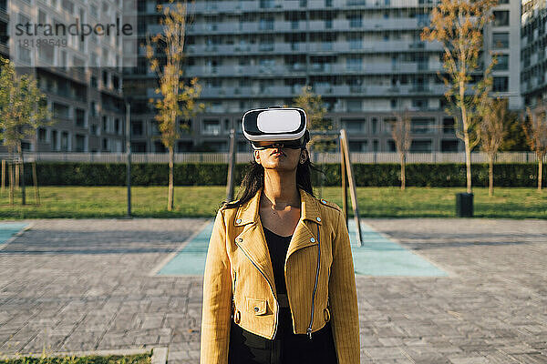 Frau mit Virtual-Reality-Simulator steht vor Gebäude