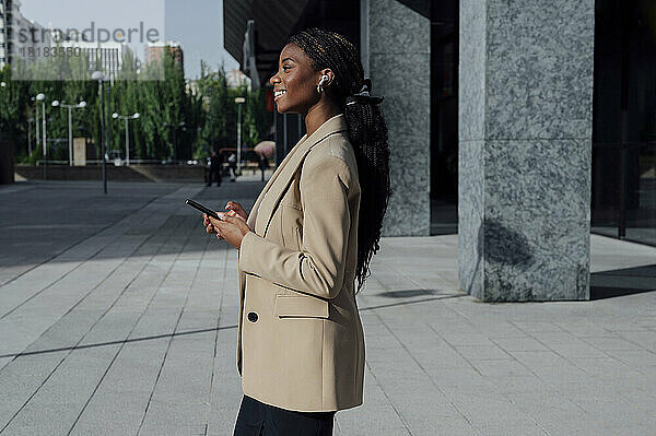 Nachdenkliche Geschäftsfrau steht mit Mobiltelefon auf Fußweg
