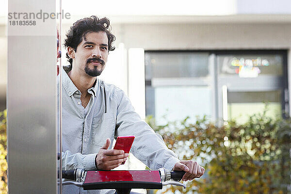 Nachdenklicher Mann mit Smartphone  der am Bahnhof ein Fahrrad mietet