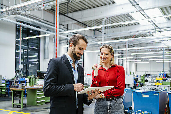 Lächelnde Geschäftskollegen mit Tablet-PC stehen in der Produktionshalle