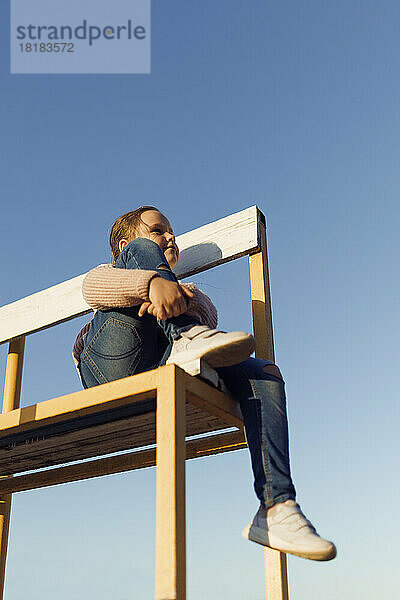 Nettes Mädchen sitzt auf einer Holzbank unter blauem Himmel
