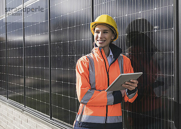Glückliche Ingenieurin mit Tablet-PC  der sich auf Sonnenkollektoren stützt