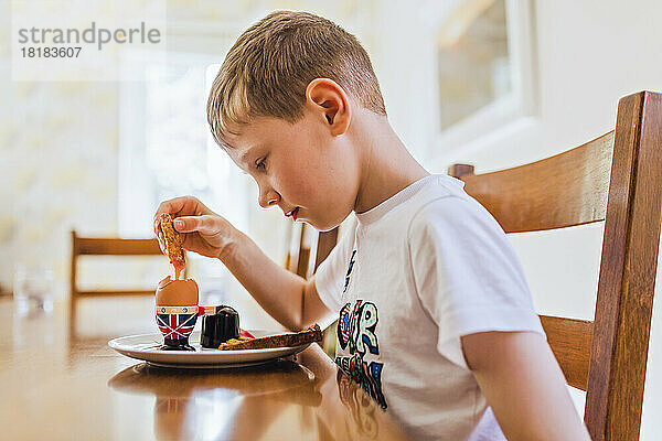 Großbritannien  trauriger Junge sitzt am Frühstückstisch und isst gekochtes Ei