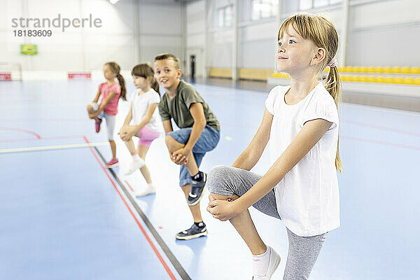 Mädchen streckt Bein mit Schülern auf dem Schulsportplatz