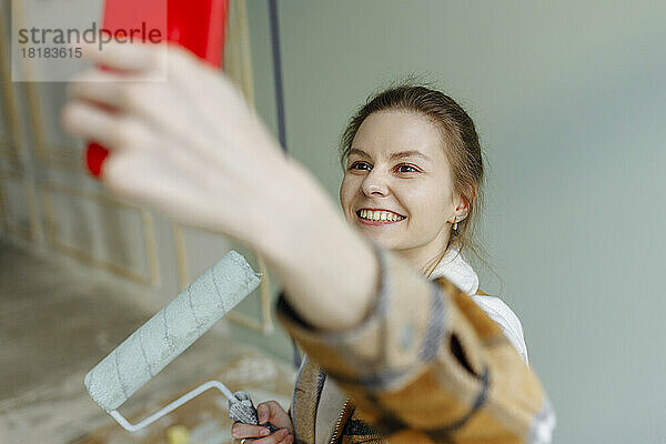 Lächelnde Frau mit Farbroller macht zu Hause ein Selfie mit dem Smartphone