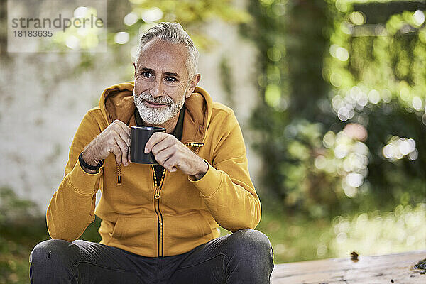Nachdenklicher reifer Mann sitzt mit Kaffeetasse im Park