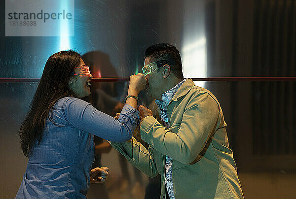 Happy mature couple wearing smart glasses punching each other by metal wall