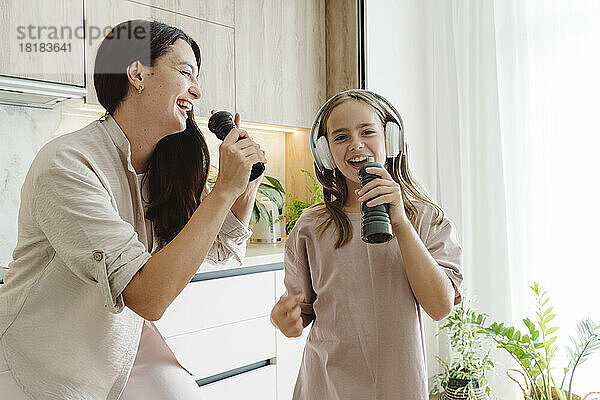 Glückliches Mädchen mit Mutter  die in Pfeffermühlen singt und in der Küche genießt
