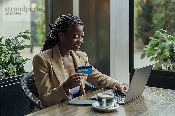 Junge Geschäftsfrau bezahlt mit Kreditkarte über Laptop im Café
