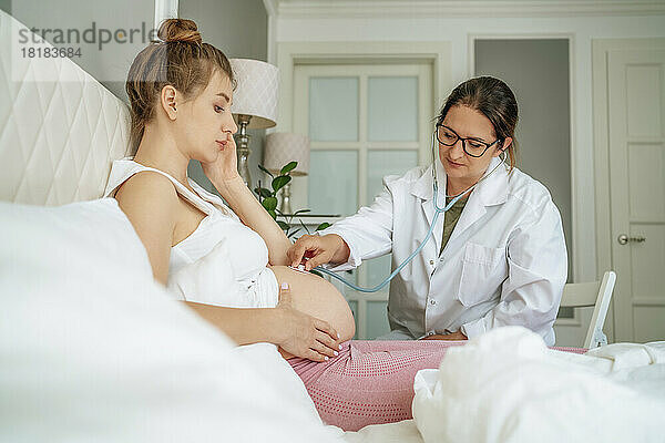 Arzt untersucht schwangere Frau  die zu Hause im Bett sitzt