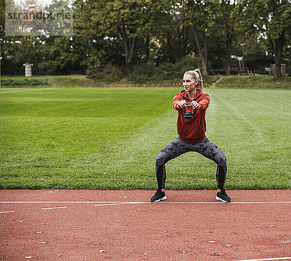 Junge Sportlerin übt mit Kettlebell auf der Laufstrecke