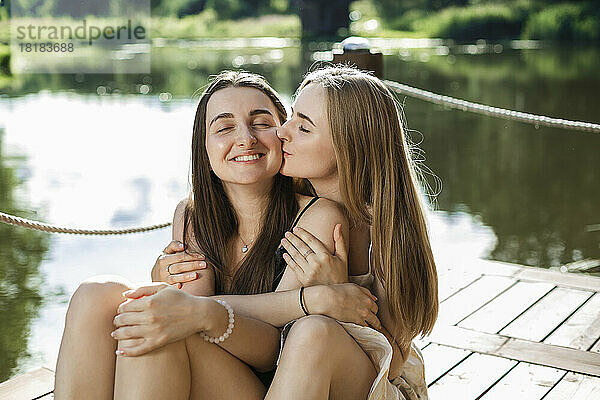 Young woman kissing friend on pier