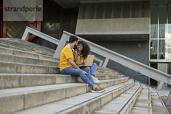 Glückliches junges Paar sitzt mit Laptop auf der Treppe
