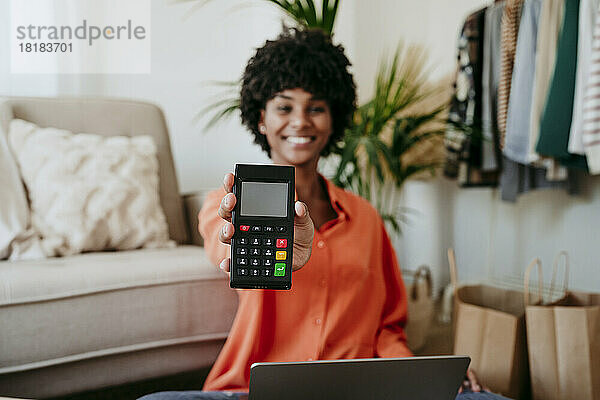 Glückliche Geschäftsfrau zeigt Kreditkartenleser im Heimbüro