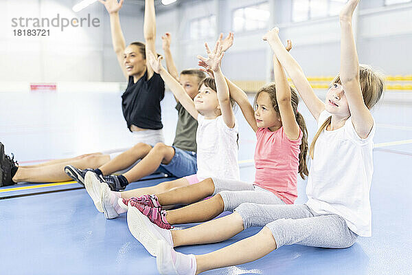 Schüler machen Übungen und sitzen mit vom Lehrer erhobenen Armen auf dem Schulsportplatz