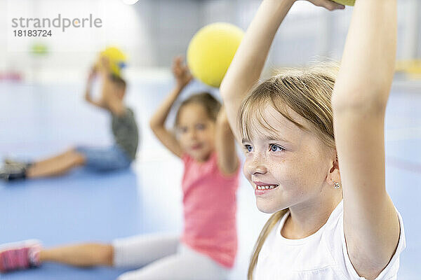 Smiling girl with arms raised by friends at school sports court