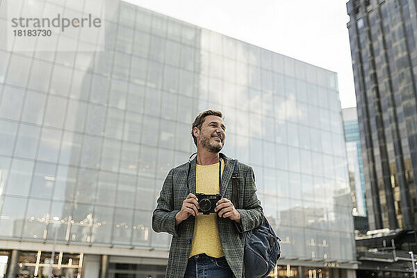 Lächelnder Mann mit Kamera steht vor dem Gebäude