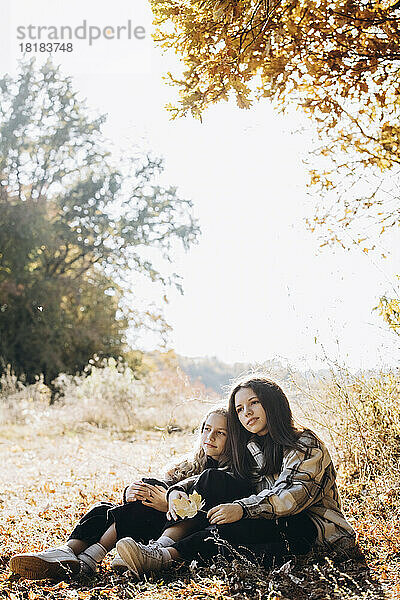 Mädchen sitzt mit Schwester im Herbstwald