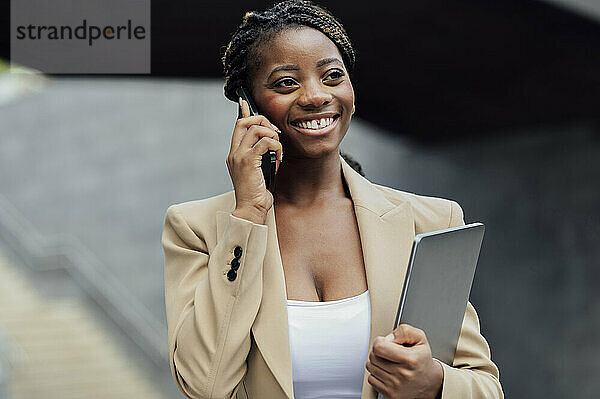 Nachdenkliche  glückliche Geschäftsfrau  die mit dem Mobiltelefon spricht und einen Laptop in der Hand hält