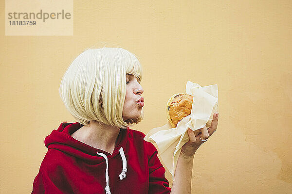 Frau knabbert an Hamburger vor pfirsichfarbener Wand