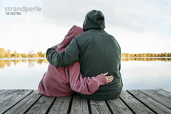 Älterer Mann umarmt Enkelin auf Steg vor See
