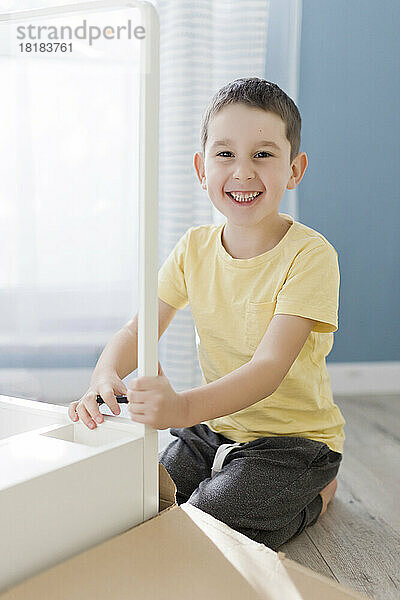 Smiling boy kneeling by table at home