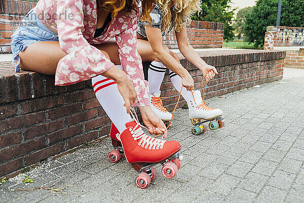 Frauen sitzen an der Wand und binden Schnürsenkel von Rollschuhen