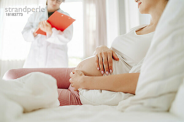 Schwangere Frau berührt den Bauch  der zu Hause im Bett liegt
