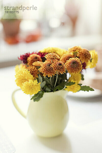 Yellow and orange chrysanthemum flowers in pitcher on table