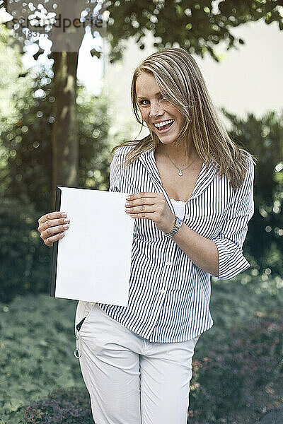 Germany  Duesseldorf  Young woman holding folder  smiling  portrait