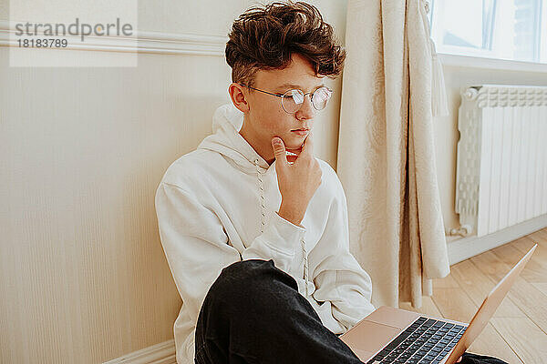 Junge mit Händen am Kinn E-Learning auf Laptop